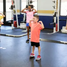 Dzieci ćwiczą z trenerem, który może prowadzić zajęcia sportowe z dziećmi. Pokazują swoje bicepsy, budując siłę i pewność siebie.