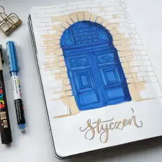 notes do rysowania: niebieskie drzwi pod łukiem z cegieł, obok pisaki i spinacz.