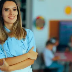 Uśmiechnięta nauczycielka w klasie, inspirująca do tego, jak zostać nauczycielem klas 1-3. Dzieci w tle.