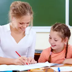 Nauczycielka z uśmiechem tłumaczy zadanie uczennicy. Zastanawiasz się, ile trwa godzina nauczania indywidualnego?