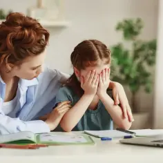 Mama pociesza płaczącą córkę, która ukrywa twarz w dłoniach. Może potrzebują wsparcia z poradni?