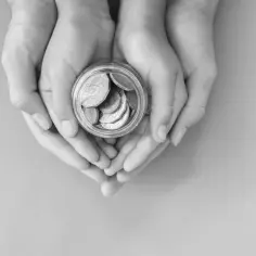 Dłonie trzymają słoik z monetami, symbolizując na co można przeznaczyć środki z dotacji, czyli katalog wydatków.