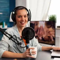 Uśmiechnięta dziewczyna w słuchawkach przy mikrofonie, tworzy podcast. To jej szkolny radiowęzeł, gdzie nagrywa ciekawe materiały.
