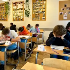 Uczniowie piszą egzamin, skupieni na zadaniach. To moment, gdy **podstawa programowa** przekłada się na konkretny **program nauczania**.