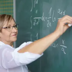 Nauczycielka matematyki pisze wzory na tablicy. Zastanawia się, kiedy najlepiej przejść na świadczenie kompensacyjne, by mieć czas na rozwój.