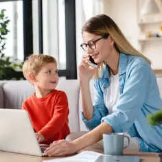 Mama na urlopie wypoczynkowym po wychowawczym pracuje przy laptopie, a synek patrzy na nią z zaciekawieniem.