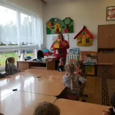 Nauczycielka czyta książkę dzieciom w punkcie przedszkolnym, tworząc atmosferę jak w przedszkolu.