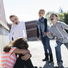 Dzieci wyśmiewają skuloną dziewczynkę. To przykład, czym jest bullying.