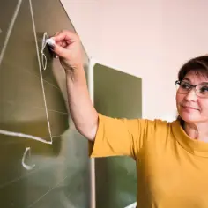 Nauczycielka pisze kredą na tablicy. Taka osoba, jak ona, może pracować w świetlicy szkolnej, pomagając dzieciom w nauce.