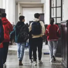 Uczniowie w szkolnym korytarzu, z plecakami, idący w stronę, kiedy składa się papiery do liceum.