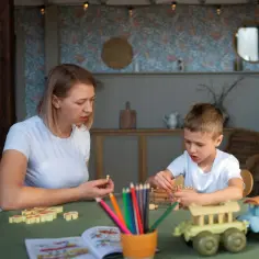 Kobieta i chłopiec grają w gry planszowe. Na stole kolorowe kredki i zabawki. To świetna opinia wwr o wspólnej zabawie.