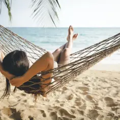 Kobieta odpoczywa w hamaku na plaży, ciesząc się dodatkowym urlopem. W tle widać morze i palmy.