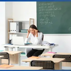 Nauczycielka z bólem głowy przy laptopie w klasie. Tablica pełna wzorów matematycznych, jakby potrzebowała dodatku funkcyjnego do rozwiązania problemu.