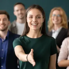 Uśmiechnięta kobieta wyciąga rękę do uścisku. W tle zespół ludzi, gotowych do podjęcia pracy, jest zobowiązany do wspólnego działania.