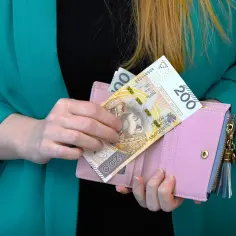 Ręka wkłada banknot 200 zł do różowego portfela. Czy to dodatek motywacyjny, czy może przygotowanie na zwolnienie lekarskie?