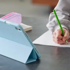 Uczeń pisze w zeszycie, korzystając z tabletu. Tak właśnie płaci się za nauczanie indywidualne w erze cyfrowej.