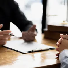 Prawnik omawia z klientem świadectwo pracy i umowę zlecenie. Na biurku dokumenty i waga sprawiedliwości.