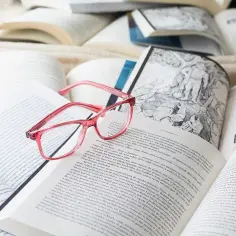 Różowe okulary leżą na otwartych książkach, symbolizując naukę zintegrowaną i dostęp do wiedzy.