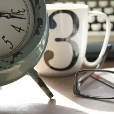 Zegar, kubek z cyfrą 3 i okulary na biurku. Czas na obliczenie wzoru na uśrednienie etatu nauczyciela.