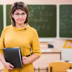 Nauczycielka w żółtej sukience z teczką w ręku, gotowa do prowadzenia rewalidacji w szkole.