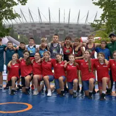 Młodzi zapaśnicy z klasy sportowej w podstawówce pozują do zdjęcia na macie. W tle Stadion Narodowy.