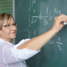 Nauczycielka matematyki pisze wzory na tablicy. Dziś godzina czarnkowa zniesiona, więc lekcja przebiega sprawnie.