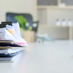Stos dokumentów, w tym dokumenty regulujące pracę przedszkola, czeka na biurku. Obok leży długopis.