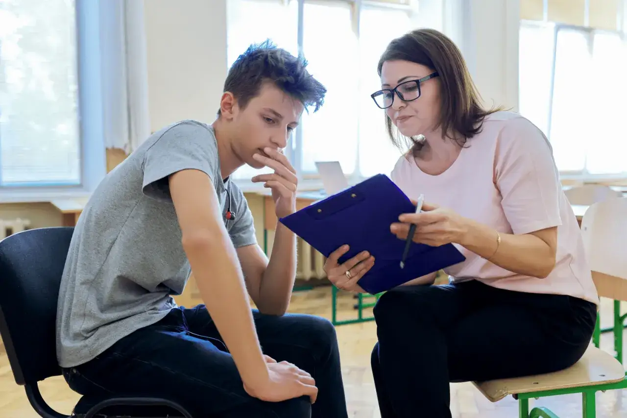 Pedagog, kto to? Kobieta w okularach rozmawia z chłopcem, trzymając teczkę.