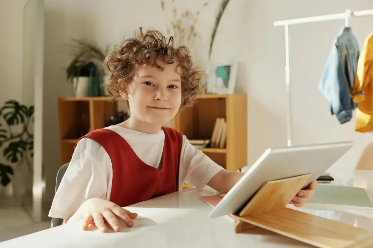 Chłopiec z kręconymi włosami uśmiecha się, trzymając tablet. To pokazuje, jak płaci się za nauczanie indywidualne online.