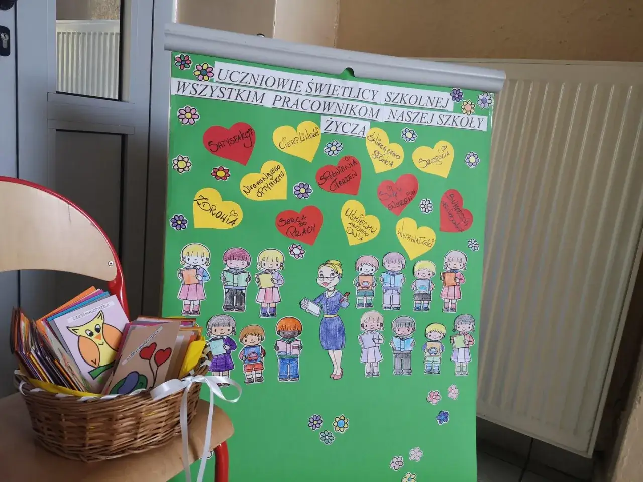 Uczniowie świetlicy szkolnej przygotowali laurkę z serduszkami życzeń dla nauczyciela, a obok koszyk z kartami 