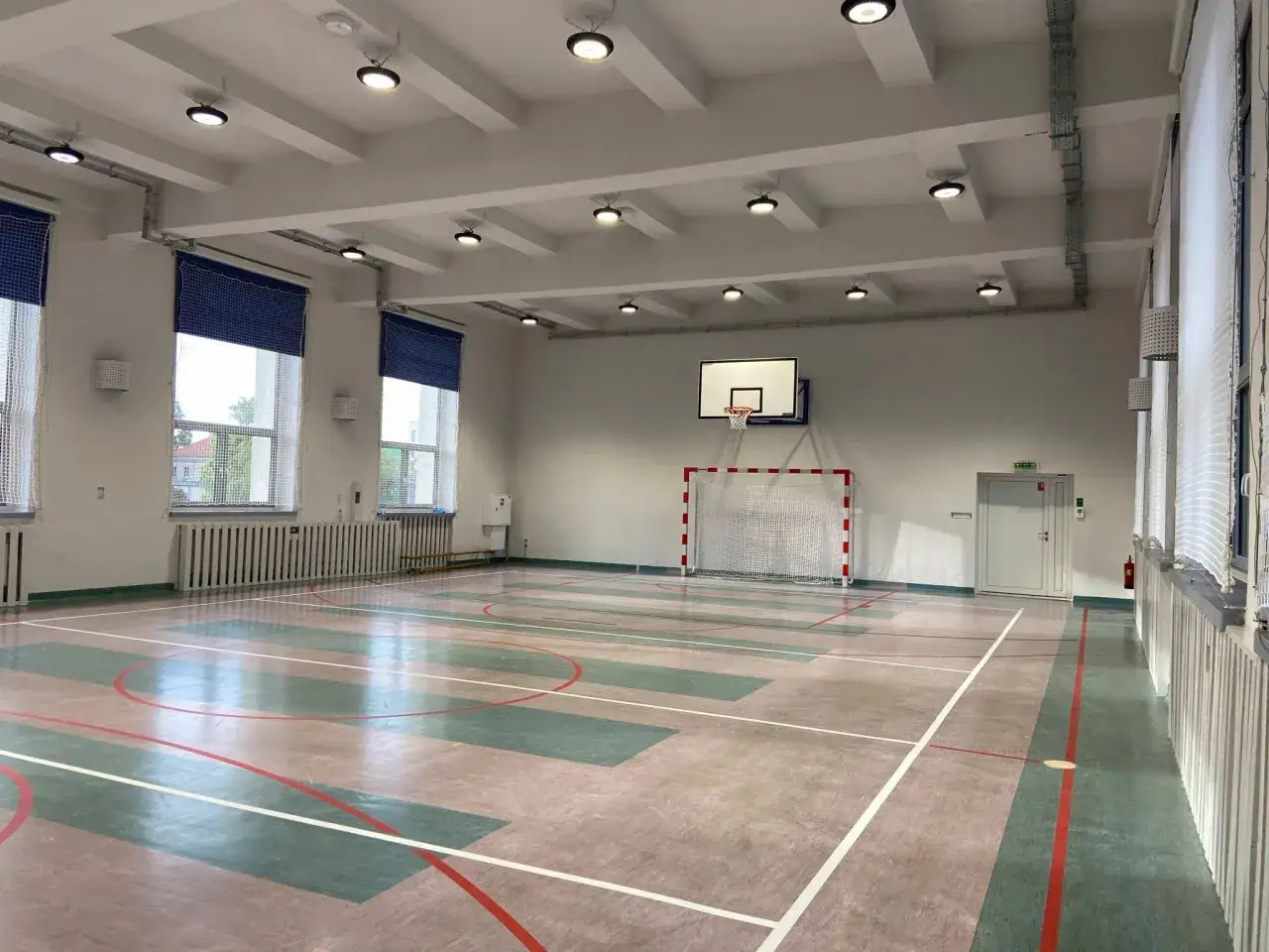 Pusta sala gimnastyczna z boiskiem do koszykówki i bramką do piłki ręcznej. Idealne miejsce na zajęcia, które nie wymagają klasyfikowania z wf.