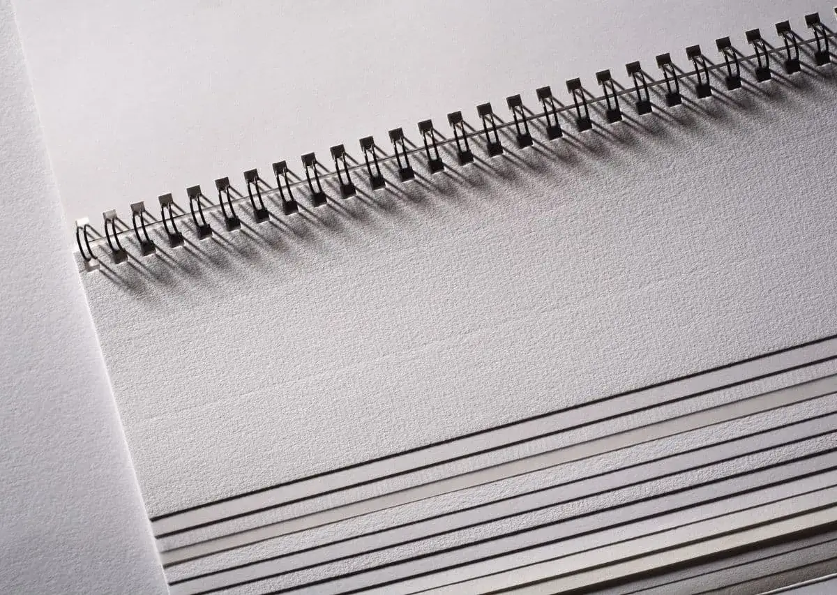 Stos kartek papieru w notatniku, widoczna grubość kartki papieru i metalowa spirala.