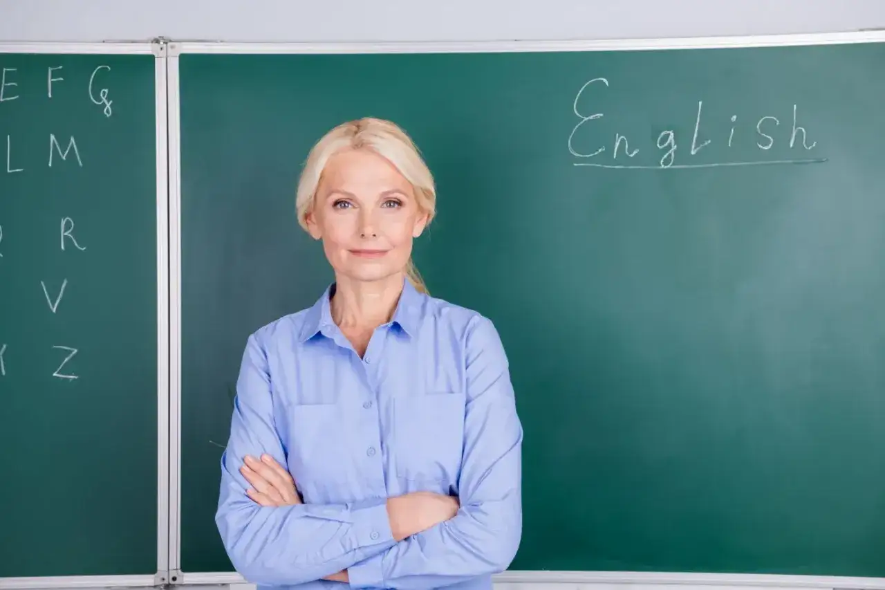 Nauczycielka angielskiego z uśmiechem przy tablicy, zastanawia się, kiedy najlepiej przejść na świadczenie kompensacyjne.
