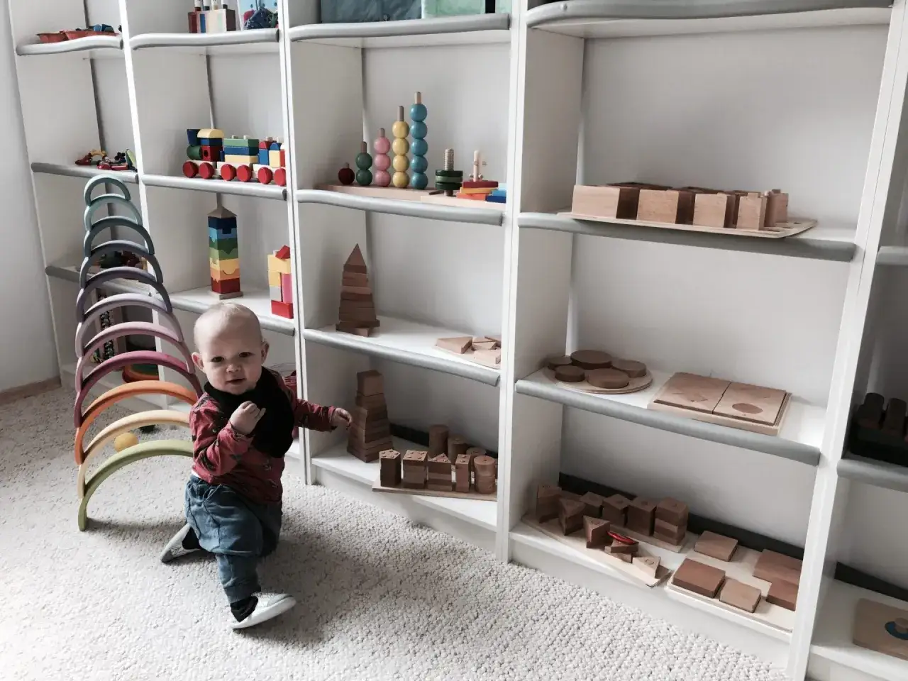 Chłopiec bawi się drewnianymi zabawkami na półkach, zgodnie z zasadami metody Montessori.