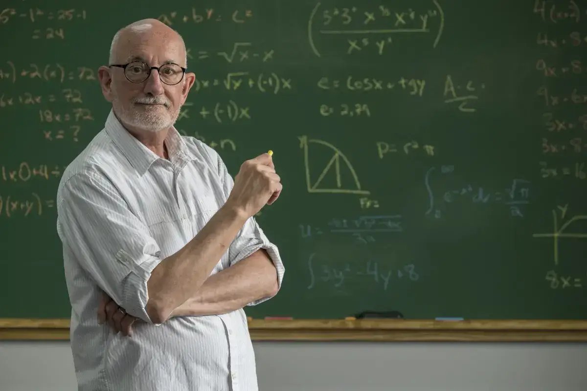 Nauczyciel emeryt, który wrócił do pracy, wyjaśnia matematyczne równania na tablicy.