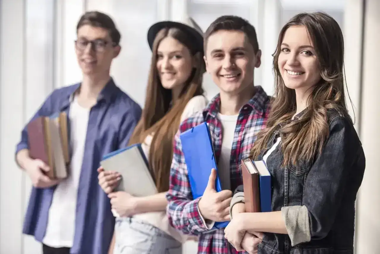 Uśmiechnięci młodzi ludzie z książkami. Czy studia podyplomowe dają status studenta? Z pewnością zdobywanie wiedzy to zawsze dobry pomysł.