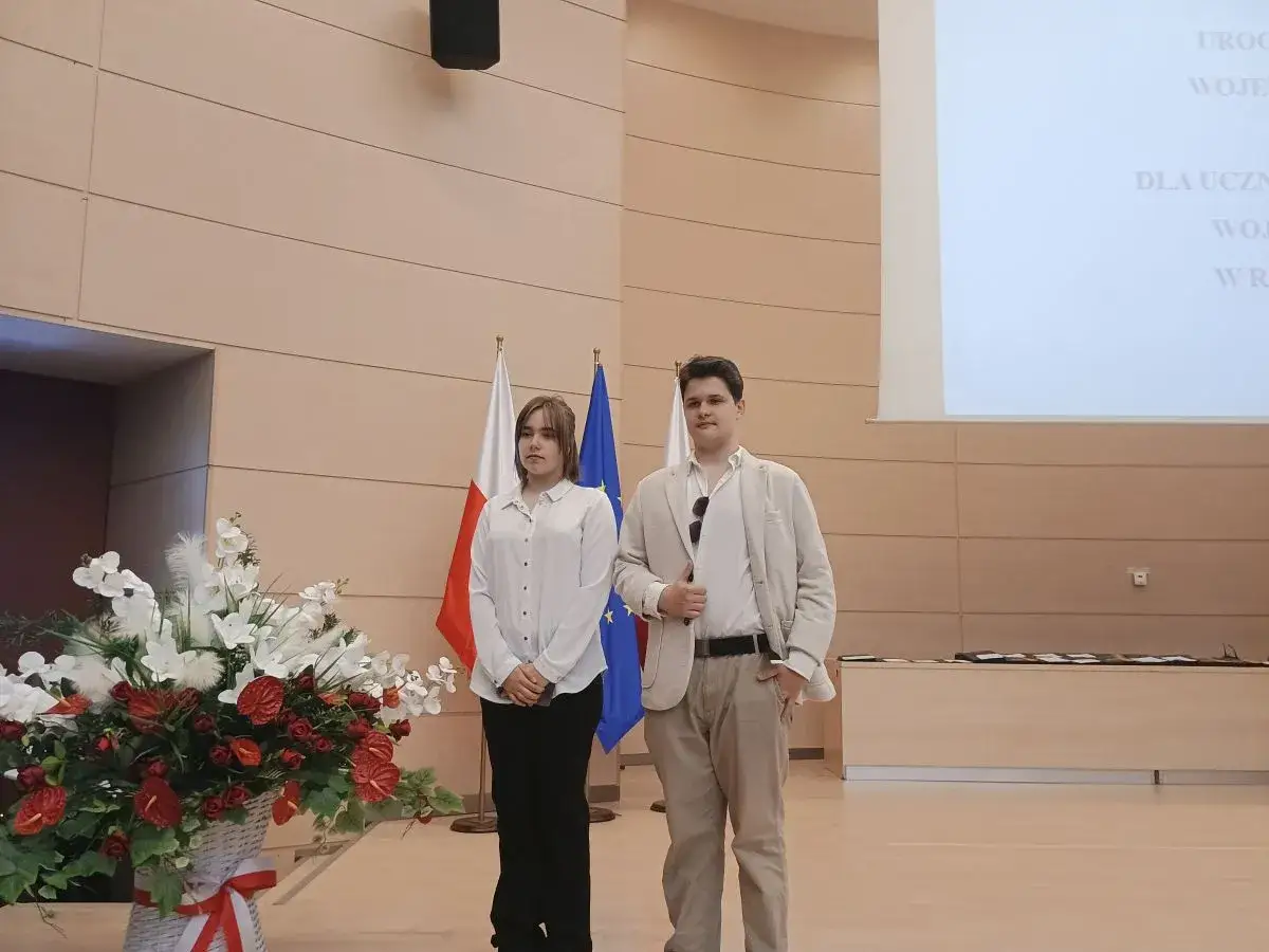 Młodzi laureaci stoją obok flag Polski i UE, gotowi odebrać nagrody.