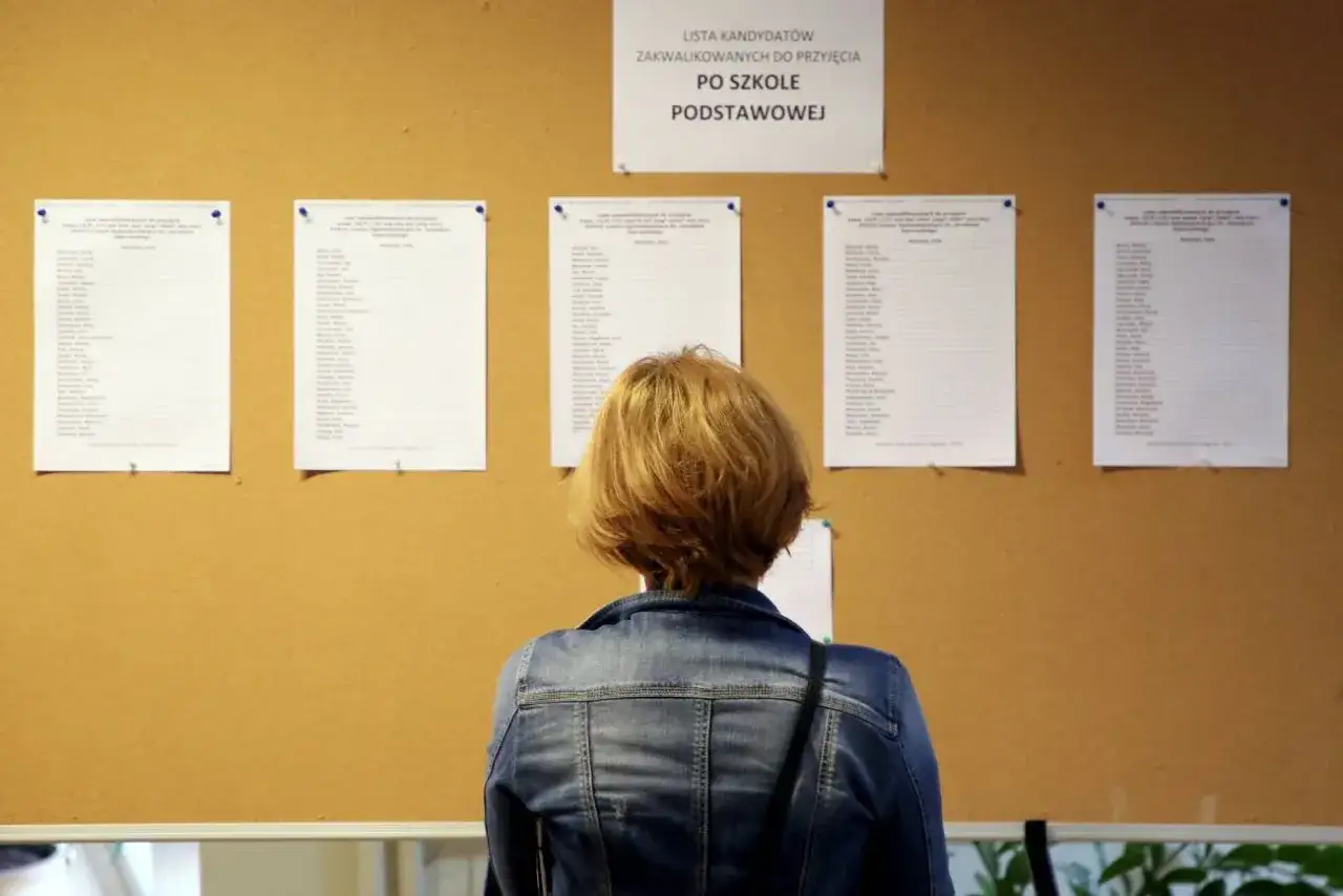 Kobieta w dżinsowej kurtce przegląda listę zakwalifikowanych kandydatów do szkół ponadpodstawowych. Nabór uzupełniający trwa.