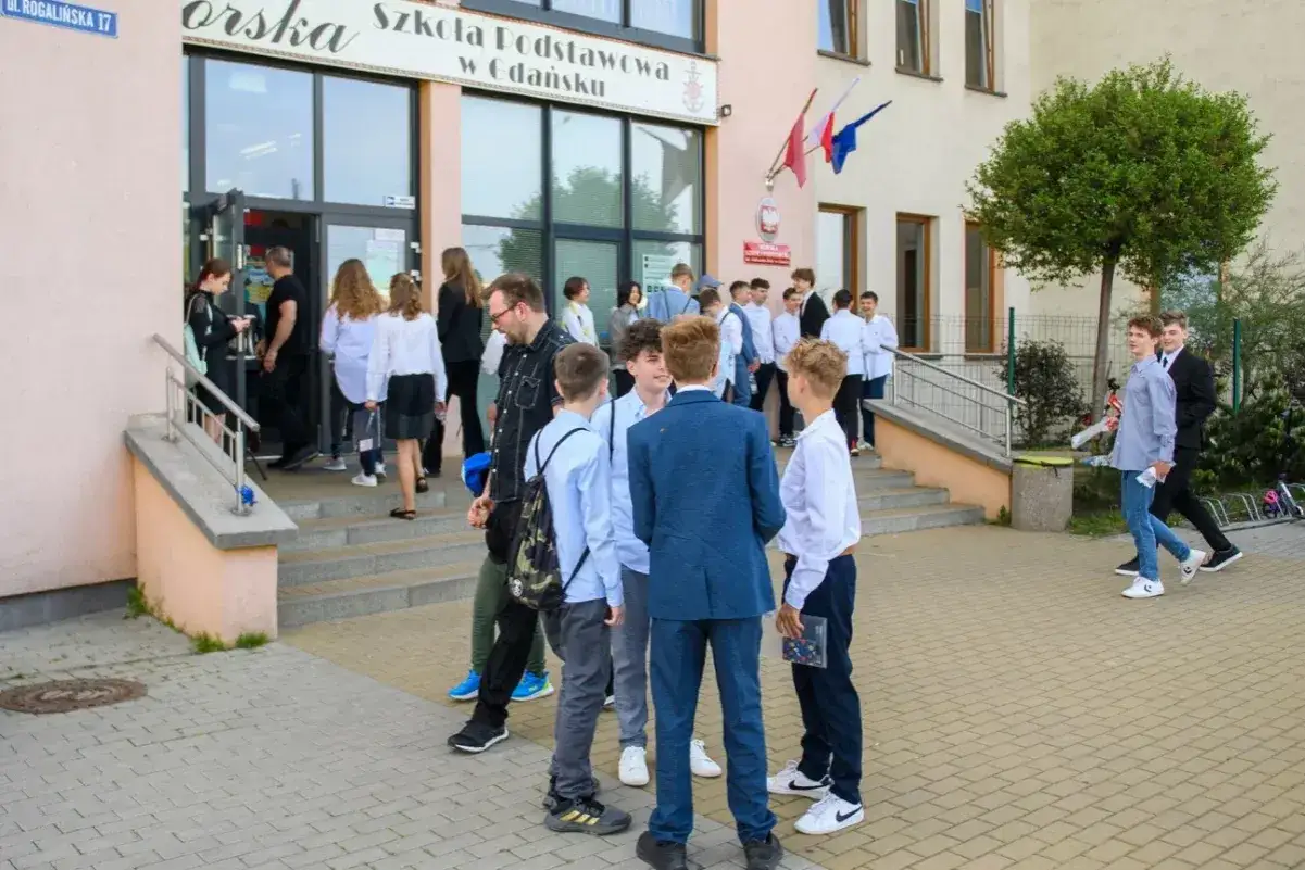 Uczniowie w białych koszulach i garniturach przed szkołą, jak wygląda rekrutacja do liceum.